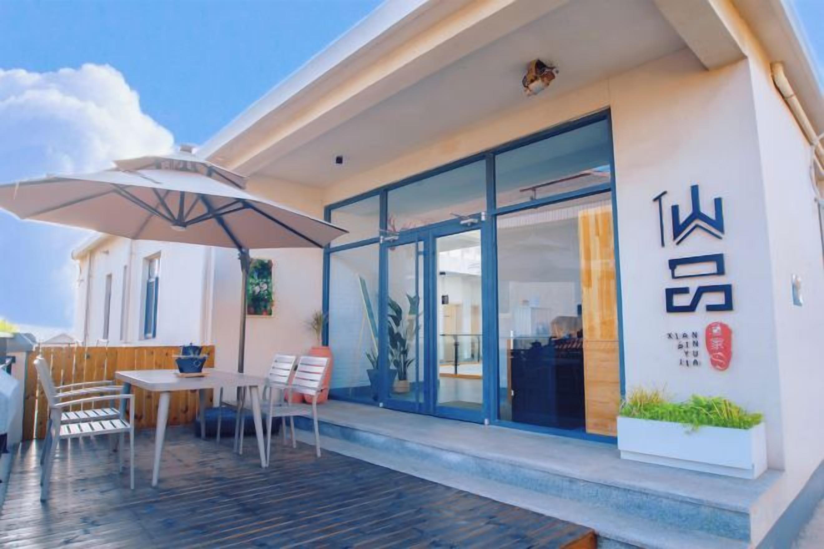 A modern building with a covered outdoor seating area, a large umbrella, and a visible entrance.