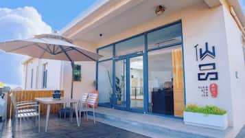 A modern building with a covered outdoor seating area, a large umbrella, and a visible entrance.