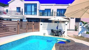Une piscine avec une terrasse en bois, une clôture blanche et une table entourée de chaises.