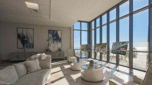 Amplia sala de estar con un ventanal con vista a la playa, que incluye un sofá, mesas auxiliares y obras de arte.
