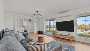 A modern living room with a large TV, a sofa, and a dining table. - 60 Beach Road, Goolwa South (Goolwa South)