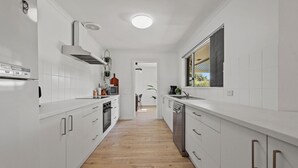 A modern kitchen with white cabinetry, a wooden floor, and a view into the dining area. - 60 Beach Road, Goolwa South (Goolwa South)