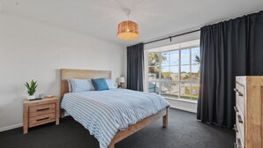 A bedroom with a bed, bedside table, lamp, and a view of the outdoors. - 60 Beach Road, Goolwa South (Goolwa South)