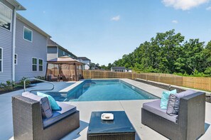 A backyard with a swimming pool, wicker furniture, and a wooden fence.