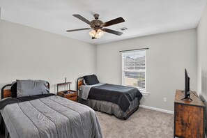 A bedroom with two beds, a ceiling fan, a window with blinds, and a TV on a wooden stand. - Charming 4-bedroom house in peaceful North Augusta (North Augusta)