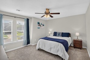 A bedroom with a bed, a ceiling fan, a nightstand, and a window with blinds.