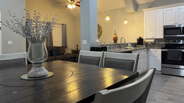 A modern kitchen with white cabinets, a granite countertop, and stainless steel appliances. There is a dining area with a dark wooden table and chairs.