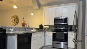 A modern kitchen with white cabinets, stainless steel appliances, a granite countertop, and a dishwasher.