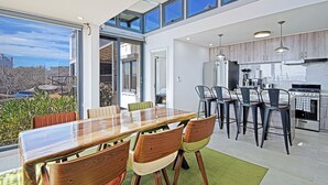 A modern kitchen with a large island, a dining area with a wooden table and chairs, and a view of the outdoors through large windows. - Funnest house in Baja! Game nights w/ smart darts, shuffleboard, & video games. Enjoy a new 8 person hot tub, lounge on multiple decks w/ firepits, fast Wifi ( 250 mb+)w/ Starlink backup. Use of 2 SUPs.  Daily housekeeping optional. (El Sargento)
