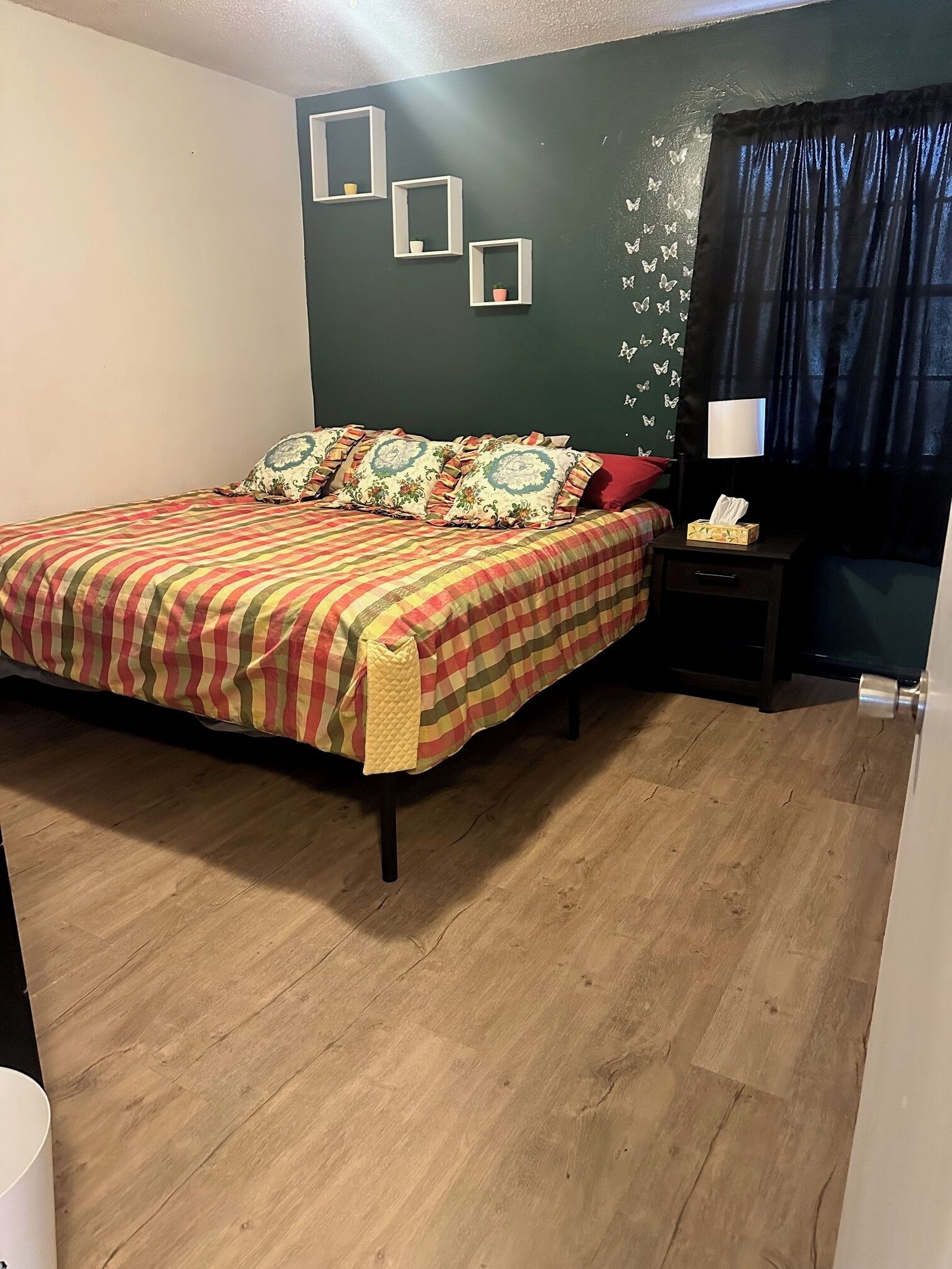 A bedroom with a bed, a nightstand, a lamp, and a wall with butterfly decals.