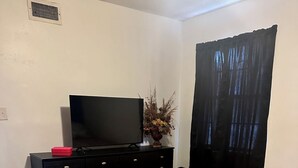 A bedroom with a bed, a dresser, a television, a vase with flowers, a window with curtains, and a white trash bin. - Charming old 3-bedroom with WiFi, & central heat & air in Cabot. NEWLY Renovated (Cabot)