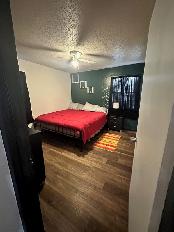 A bedroom with a bed, a ceiling fan, a dresser, and a window with curtains.
