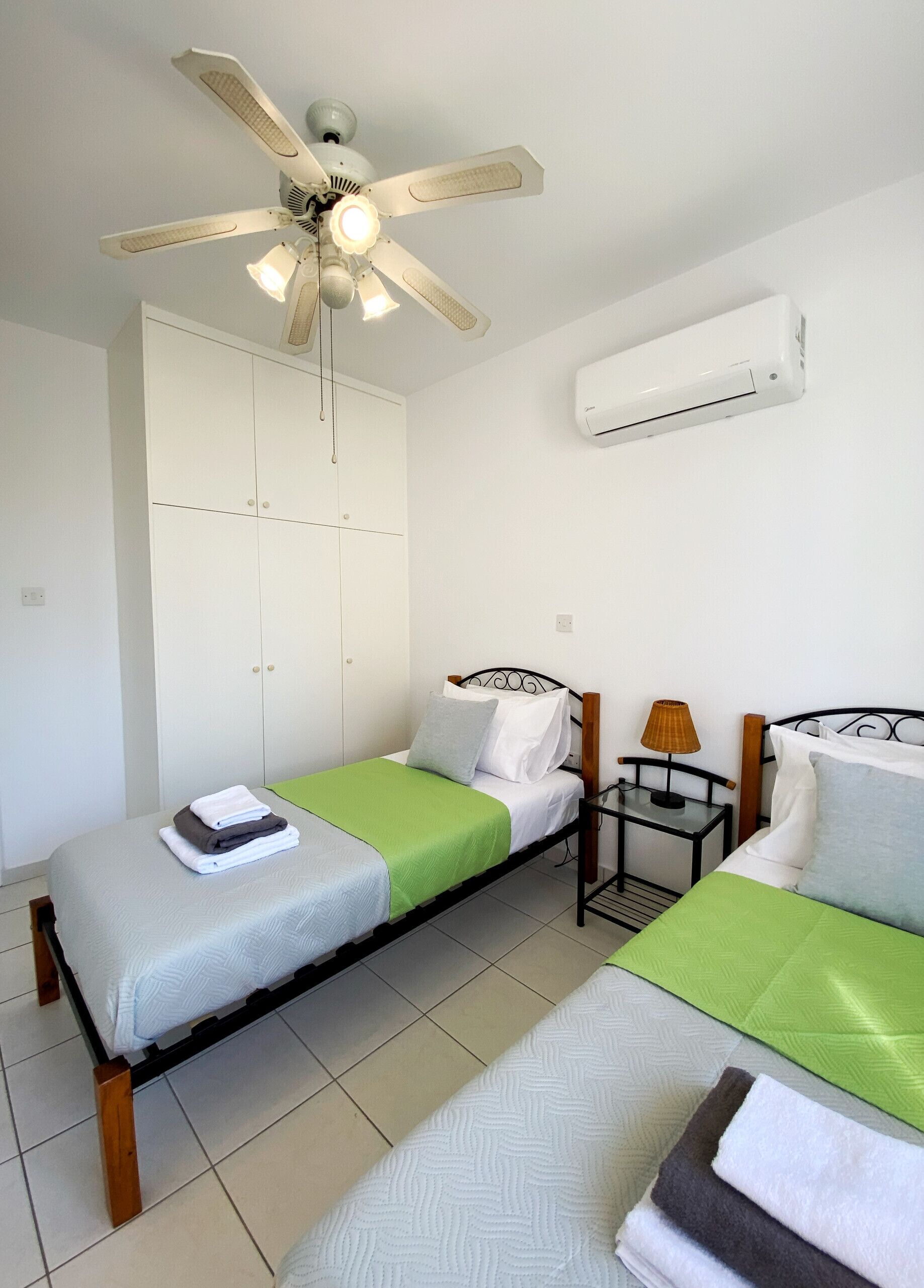 A bedroom with two single beds, a ceiling fan, an air conditioning unit, and a wardrobe.