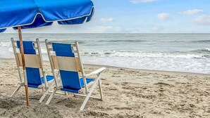 Une scène de plage avec un parasol bleu et deux chaises de plage donnant sur l’océan.