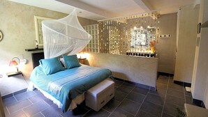 A bedroom with a bed, bedside tables, a nightstand, a bedside lamp, a window with curtains, and a bathroom with a sink and mirror. - Country house at Le Barroux, Mont-Ventoux, air-conditioning, pets allowed (1) (LE BARROUX)