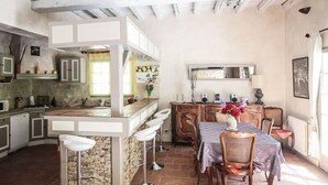 A kitchen with a central island, bar stools, a dining table with chairs, and a stone wall. - Country house at Le Barroux, Mont-Ventoux, air-conditioning, pets allowed (1) (LE BARROUX)