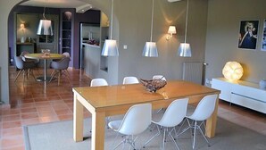 A modern dining area with a glass-top table, white chairs, pendant lights, and a decorative bowl centerpiece. - In Violès, Vaucluse, exceptional vacation home, air-conditioned, heated pool. (VIOLÈS)