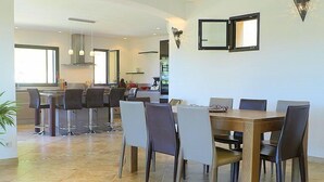 A modern dining area with a wooden table and chairs, a kitchen in the background, and a large window providing natural light. - Air-conditioned villa in Montfort-sur-Argens, Var, private pool. (MONTFORT-SUR-ARGENS)