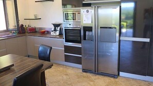 A modern kitchen with a stainless steel refrigerator, oven, and microwave. There is a dining table with chairs and a window with a view of greenery. - Air-conditioned villa in Montfort-sur-Argens, Var, private pool. (MONTFORT-SUR-ARGENS)