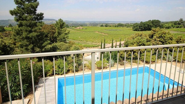 Une piscine avec vue sur un vignoble et des collines lointaines.