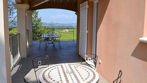 Une terrasse extérieure avec une table ronde et des chaises, un espace couvert offrant une vue sur le paysage, et un bâtiment à l’extérieur de couleur pêche.
