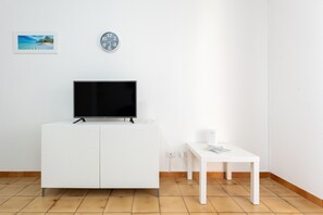 A white TV stand with a flat-screen TV, a small table with a cup, a clock, and a framed picture on the wall.