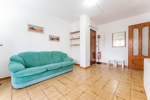 A room with a teal sofa, tiled floor, white walls, a wooden door, and a small white table.