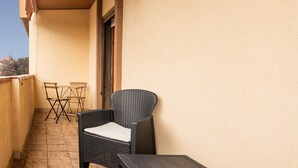 A balcony with a wicker chair, a small table, and a folding chair.