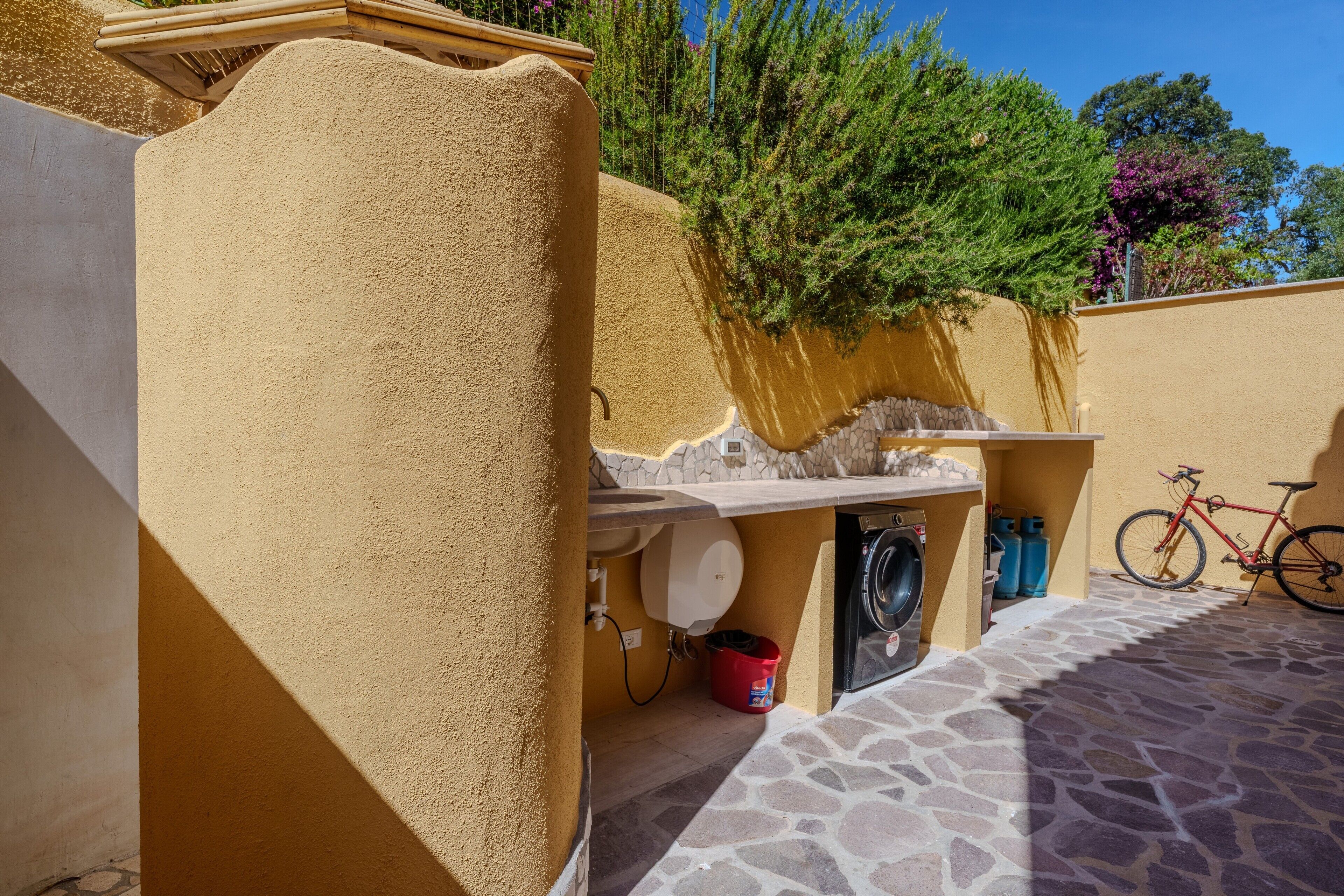 A laundry area with a washing machine, a red bucket, and a bicycle.