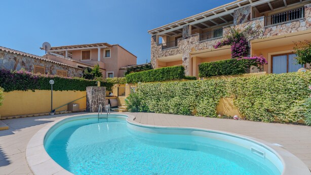 A swimming pool surrounded by a stone wall, a yellow building, and a stone building with balconies. - Apartment 'Avocado' with Shared Pool, Private Garden & Air Conditioning (Maltineddu)