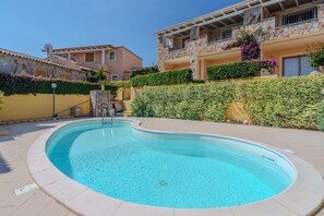 Una piscina rodeada por un muro de piedra, un edificio amarillo y un edificio de piedra con balcones.