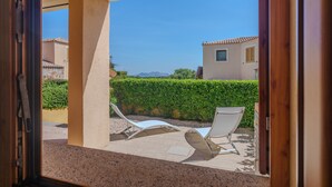 A view through an open door to a balcony with two lounge chairs, a beige wall, and a hedge in the background. - Apartment 'Avocado' with Shared Pool, Private Garden & Air Conditioning (Maltineddu)