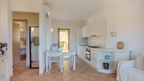 A compact kitchen with white cabinets, a dining table with chairs, a small stove, and a sink. - Apartment 'Avocado' with Shared Pool, Private Garden & Air Conditioning (Maltineddu)