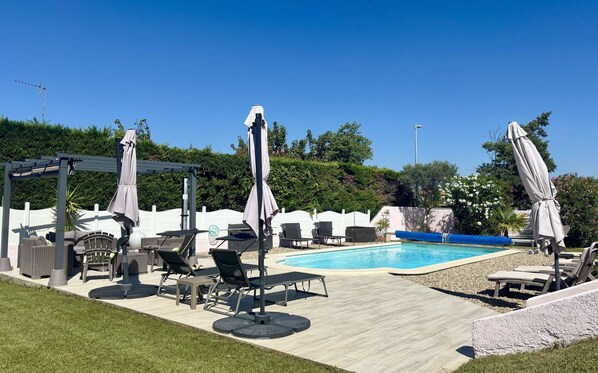 A pool area with lounge chairs, umbrellas, and a pergola.
