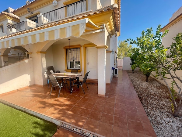 Un patio con una mesa y sillas de comedor, un pequeño jardín y un edificio con balcón.