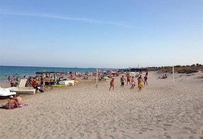 Una playa con gente, sombrillas y barcos.