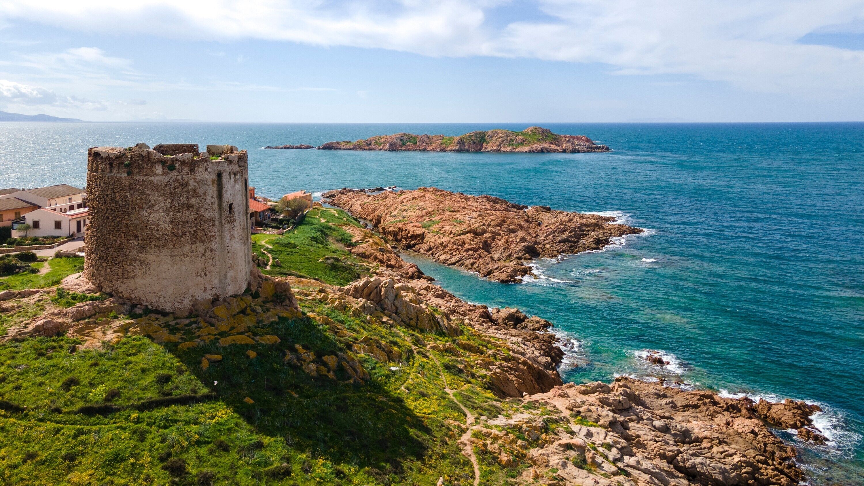 Eine Küstenlandschaft mit einem historischen Steinturm, felsigem Gelände und einer kleinen Insel in der Ferne.
