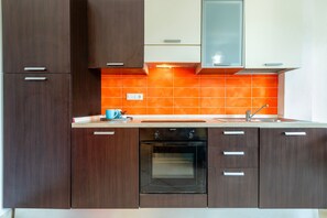 Une cuisine moderne avec des meubles de couleur bois foncé, un four noir et un pare-feu orange.