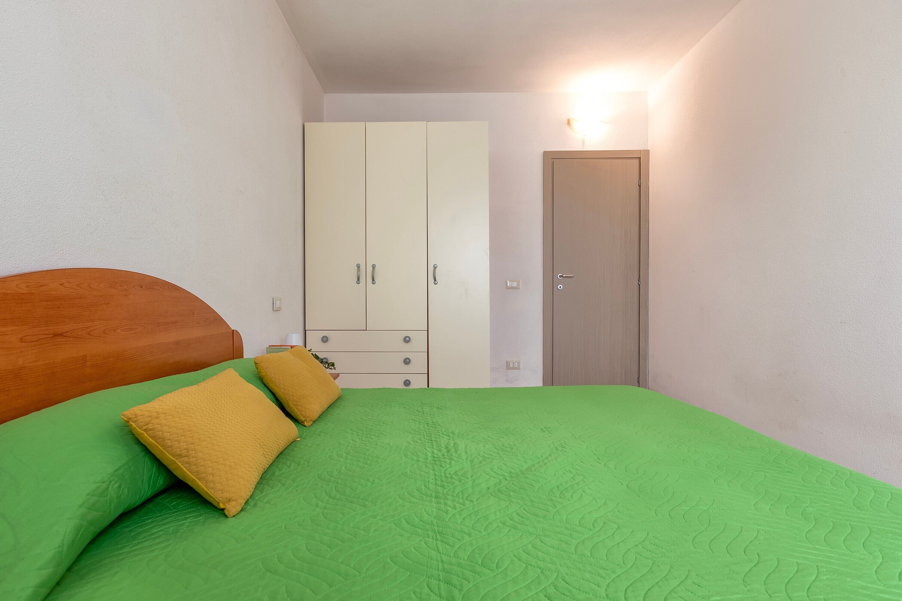 Une chambre à coucher avec un lit, une literie verte, une armoire et une porte.
