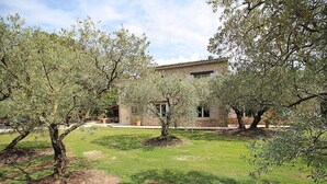 A stone building with a tiled roof, surrounded by olive trees and a grassy lawn. - Stone landhouse in scenic garden, heated pool, in L'Isle-sur-la-Sorgue. (L'ISLE-SUR-LA-SORGUE)