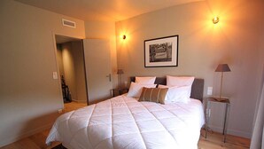 A bedroom with a large bed, two bedside tables, a framed picture on the wall, and a door leading to another room. - Stone landhouse in scenic garden, heated pool, in L'Isle-sur-la-Sorgue. (L'ISLE-SUR-LA-SORGUE)