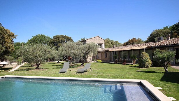 A swimming pool with lounge chairs, a stone house, and olive trees in the background. - Stone landhouse in scenic garden, heated pool, in L'Isle-sur-la-Sorgue. (L'ISLE-SUR-LA-SORGUE)