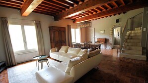 A spacious living room with a large white sofa, a dining area with a wooden table, and a staircase leading to an upper level. - Stone landhouse in scenic garden, heated pool, in L'Isle-sur-la-Sorgue. (L'ISLE-SUR-LA-SORGUE)
