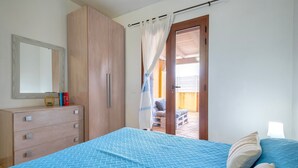 Una camera da letto con un letto, un armadio, uno specchio e una porta che dà su uno spazio esterno.