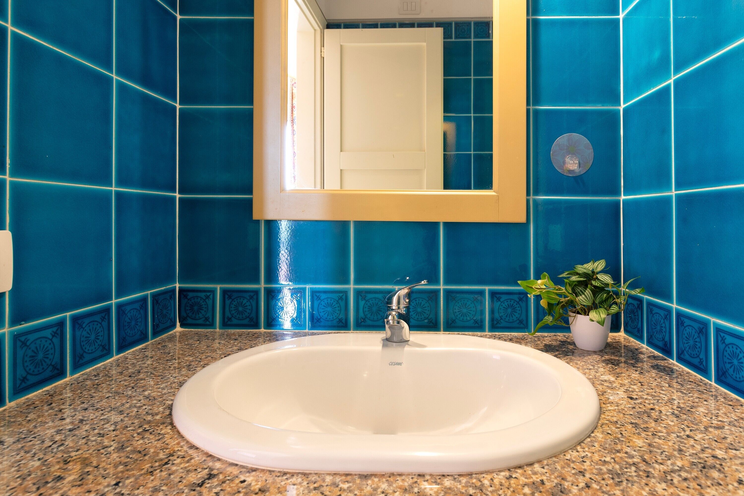 Un bagno con un lavandino bianco, piastrelle blu e una pianta in vaso.