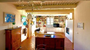 A spacious living area with a wooden dining table, a white sofa, and a kitchen in the background. - Vacation home in the Luberon in the heart of nature, private pool. (SAINT-MARTIN-DE-CASTILLON)