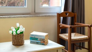A wicker basket with white flowers and a stack of books on a table by a window.