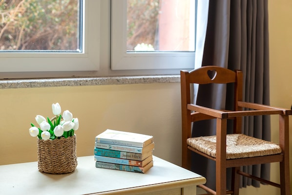 A wicker basket with white flowers and a stack of books on a table by a window.