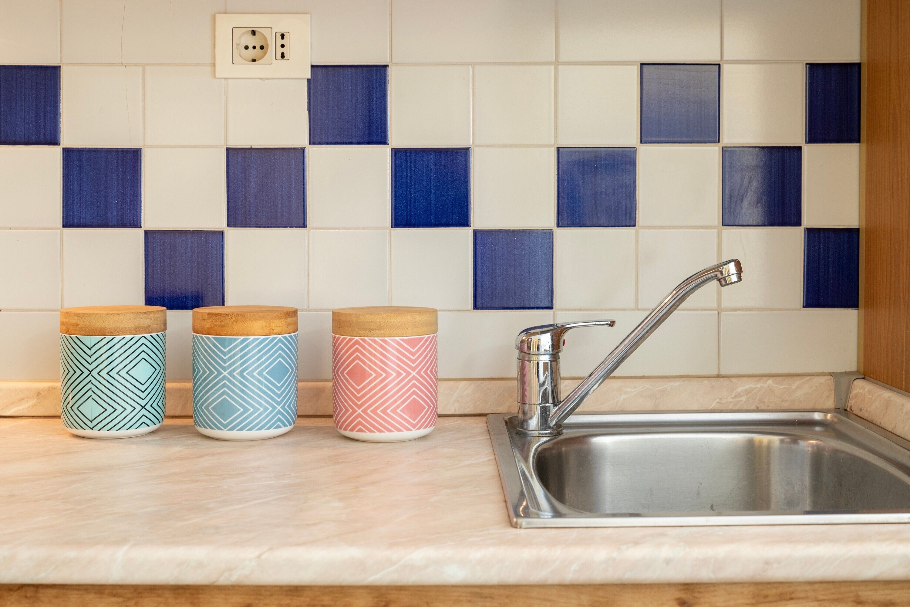 A kitchen with a sink, three patterned containers, and a tiled backsplash.