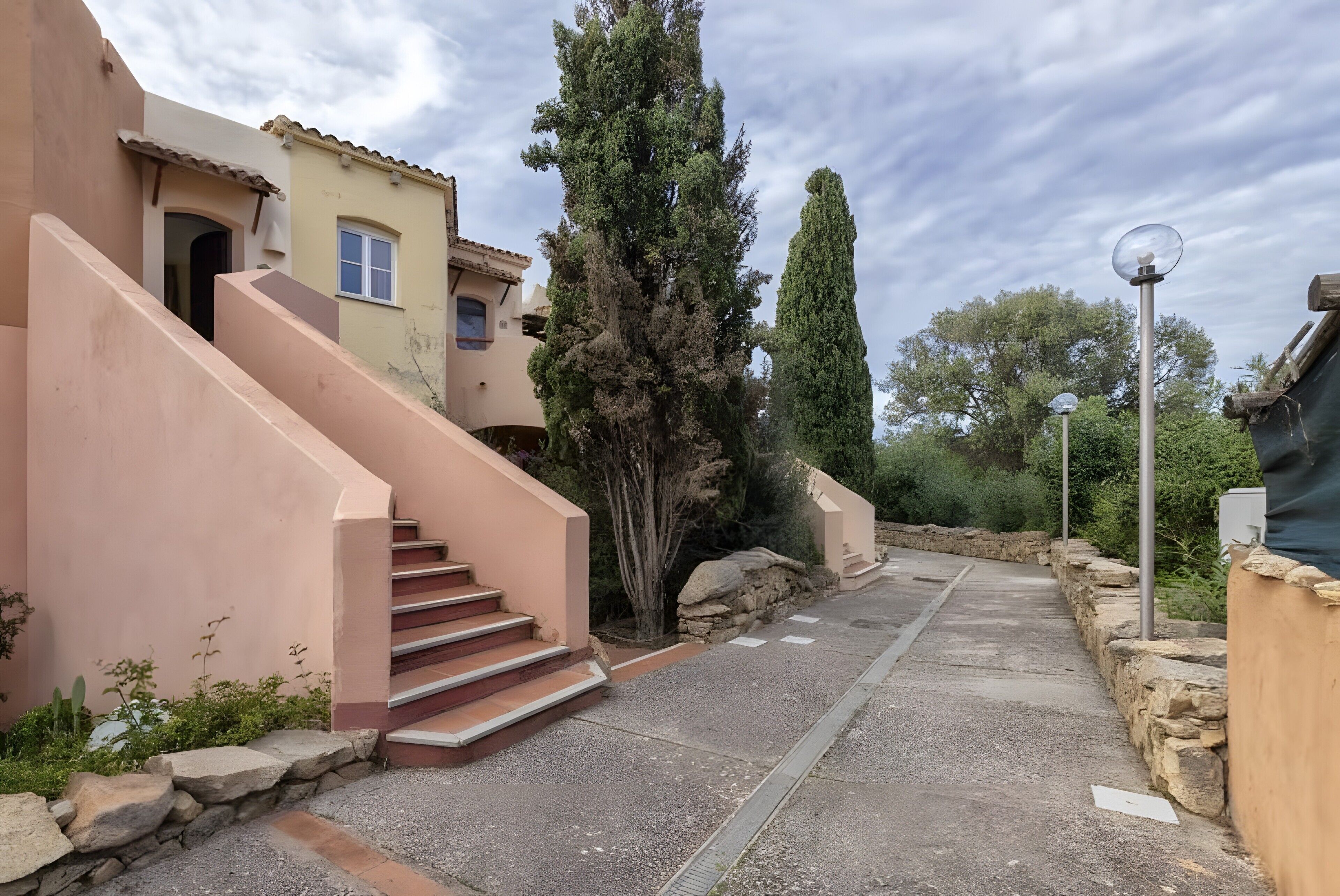 Una edificación residencial con una escalera que lleva a una puerta, un muro de piedra y un farol.